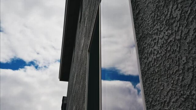 Low-angle time-lapse footage of the dense clouds rolling over an urban building with a glass window