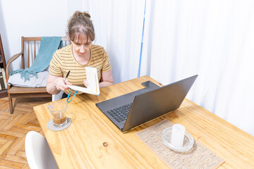 Woman over 50 multitasking with laptop, notes  and phone
