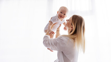 Smiling young mother holding happy baby in arms, isolated on white background, natural light, bright clean minimal style, bonding together with love and warmth, joyful parenting family