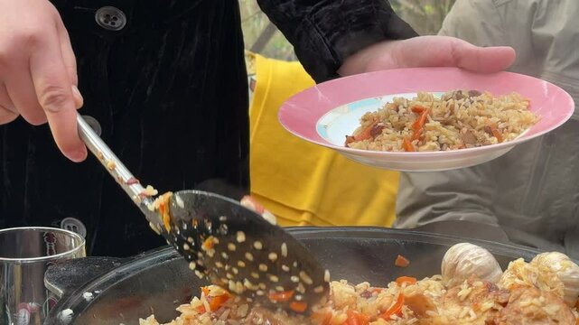 Tajik woman serving pilaf cooked in a cauldron onto plates