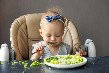 Adorable Baby Girl Enjoying Healthy Meal, Eating broccoli with spoon and Making Mess, Happy Infant, Toddler First Foods. Child eating vegetables