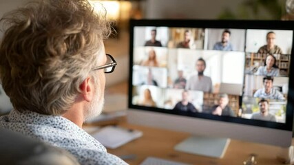 Middle-aged man with glasses watching a multi-person video call on a large monitor in a cozy home office environment, illustrating remote work and digital communication