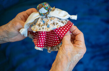Folk rag doll bell in the hands of an elderly man.Making dolls from rags using folk methods.