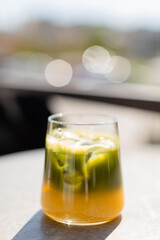 Glass of iced matcha latte on a sunlit table casting a long shadow. Bright and minimalistic composition. Refreshing healthy drink with vibrant green color, top view.