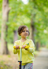 Beautiful little girl riding a scooter in the park