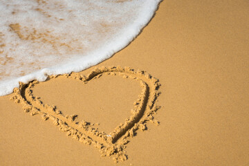 a painted heart on sea sand with flowing white sea foam