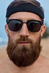 Brutal bearded male with glasses on the beach.