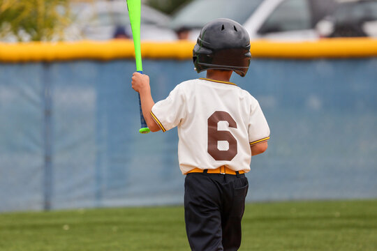 Back view of a 6 year old boy walking holding a bat.