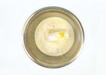 Top view of powdered sugar, cream cheese, lemon zest, and cream in a stainless steel mixing bowl, ready for making a dessert or frosting.