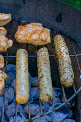 Grilled chicken pieces and sausages cooking over hot charcoal on an outdoor barbecue, with golden sear marks and a rustic metal grill.
