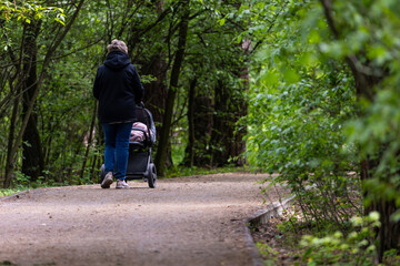 Obraz premium An elderly woman with silver hair pushes a stroller along a forested path. Maybe a grandmother or nanny out for fresh air and a peaceful walk. Moment reflects connection, caregiving, and everyday life