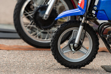 Obraz premium Small motorcycle tire resting on gravel ground beside larger bike wheels during daylight