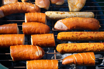Grill loaded with sausages and marinated chicken, sizzling over hot charcoal, with smoke rising in the sunlight.