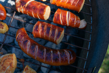 Grill loaded with sausages and marinated chicken, sizzling over hot charcoal, with smoke rising in the sunlight.