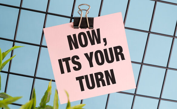 A clip board with a pink sign that says Now, it's your turn.