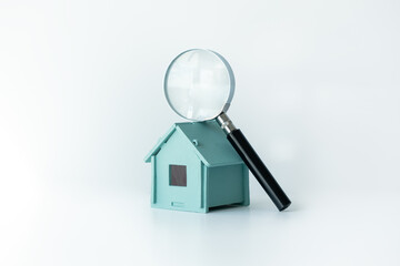 Magnifying glass highlighting a house model on a table. Real estate concept for property market,...