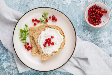 Breakfast with whole grain sandwich with cream cheese or cottage cheese, fresh mint and red berries on white plates top view
