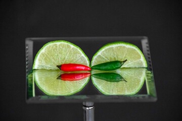 Tahiti lime cut with chili pepper on mirror with reflection