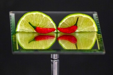 Tahiti lime cut with chili pepper on mirror with reflection