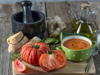 Close-up of a nice plate of cold gazpacho along with several tomatoes, toasted bread and various ingredients on a wooden table