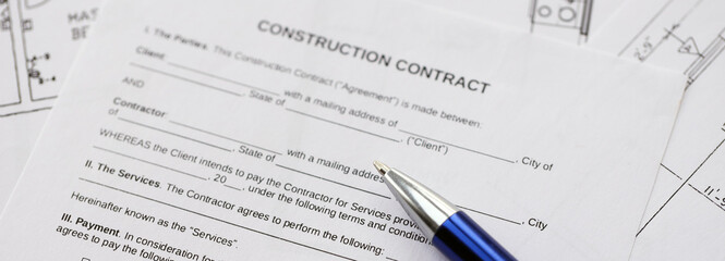 Pen on residential construction agreement and planning blueprints of residential building project...
