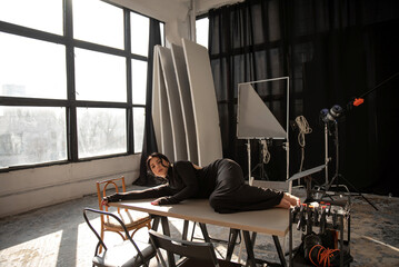 Brunette in a black dress lies on a table in the studio