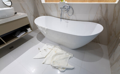 A modern freestanding bathtub in a luxury bathroom with towels left on the floor