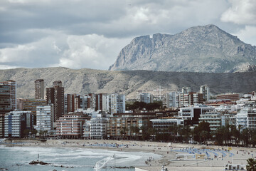 Obraz premium Seaside urban landscape with mountain backdrop and beachfront high-rise buildings