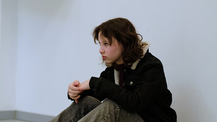 A young girl sits on the floor, holding her head in her hand with a thoughtful expression. This...