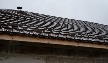 Edge of a roof made of brown metal tiles with a wooden cornice