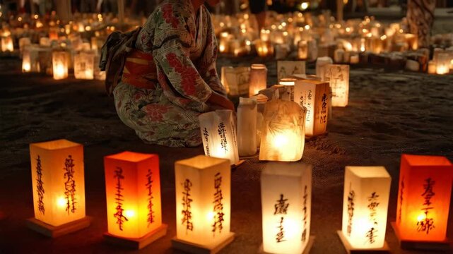 Unrecognizable person in traditional robe kneeling among lit paper lanterns on a beach during an evening ceremony or event.