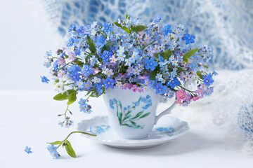 Bouquet of spring flowers forget-me-nots and omphalodes close-up in a cup on the table , blur, beautiful card