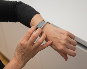 Elderly Caucasian woman looking at smart watch. Close-up of hands. 