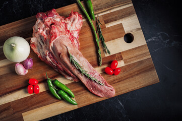 Lengua de res cruda sobre tabla de madera acompa&ntilde;ada de jitomate cherry, esparragos, chile, ajos y cebolla