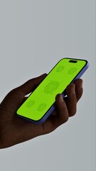 Black African-American old male using smartphone with a blank green screen. Mobile app video mockup. Vertical phone orientation