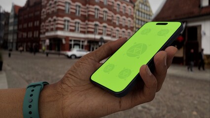 GREEN SCREEN CHROMA KEY Mobile phone with customizable screen held in hand in a lively urban plaza,...