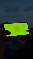 GREEN SCREEN CHROMA KEY A hand holding a smartphone with a green screen at night, overlooking the...
