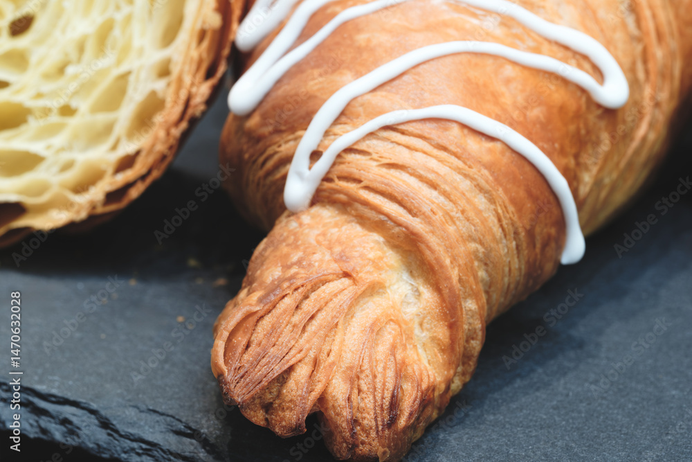 Poster a croissant with a white glaze on top sits on a black surface. the glaze is drizzled down side of th