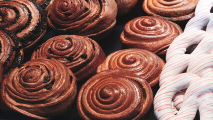 A variety of pastries, including cinnamon rolls and a donut with a white stripe, are displayed on a counter. cinnamon rolls are brown and have a spiral shape, while the donut is white.