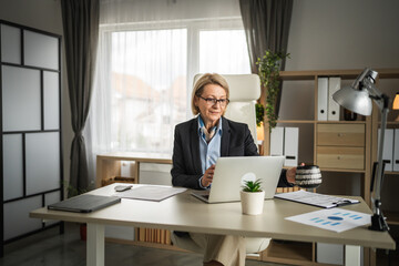 One mature woman with eyeglasses work at laptop and document at office
