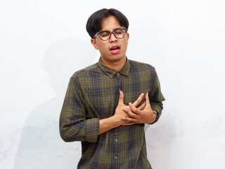 Young Asian man holding his left chest with a pained, sad expression, isolated on a white...