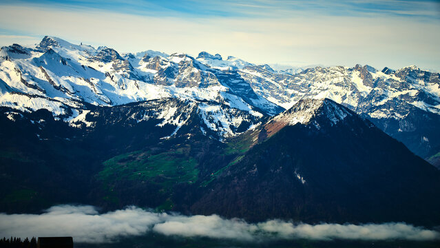 Majestic snow-capped mountains rise above serene green valleys under a clear blue sky in the Swiss Alps during midday