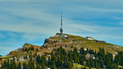 Tower and radio station on a mountain peak surrounded by lush greenery and a clear sky