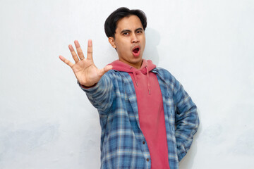Angry young Asian man with a serious expression, showing a stop gesture with his hand, representing...