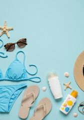 Flat-lay of beachwear essentials bikini, flip-flops, sunglasses, straw hat, and sunscreen arranged neatly on a pastel background, with copy space.