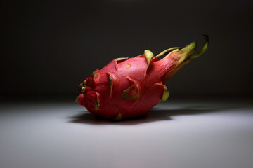 Single dragon fruit lying on neutral gray surface with soft studio lighting and minimal background...