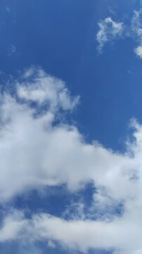 Un cielo de azul con varias nubes de color blanco y gris con un movimiento lento. Video vertical