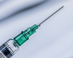 Sterile syringe with green hub and sharp needle against light background
