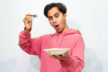 Young Asian man wearing a pink hoodie shows a happy and euphoric expression while looking at a...