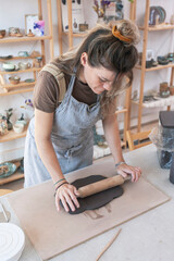 Ceramist modeling and flattening clay with roller in his studio